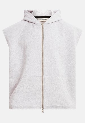 Lysegrå, ærmeløs hættetrøje med lynlås foran og kengurulomme, mærket "Redefined Rebel" indeni kraven.