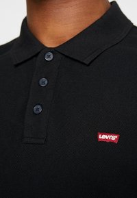 Czarna koszulka polo wykonana z teksturowanej tkaniny, z trzema guzikami w kołnierzyku oraz małym, czerwonym logo Levi's na klatce piersiowej.