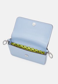 Clutch in pelle blu chiaro con chiusure in argento, aperto per rivelare un rivestimento interno giallo brillante con un motivo in bianco e nero.