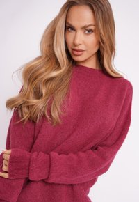 Przewymiarowany sweter typu pulower w głębokim, malinowym kolorze, wykonany z miękkiej, teksturowanej tkaniny, z prążkowanymi mankietami i dekoltem w łódkę.