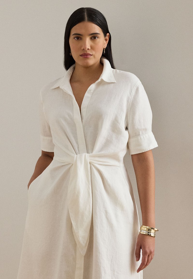 Balta lina krekla kleita ar pogām priekšpusē, īsām piedurknēm un sasienamu jostasvietu. Tai ir sānu kabatas un minimālas detaļas.