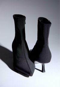 Černé vysoké kozačky na kotníky vyrobené z hladké látky, s špičatou špičkou, štíhlým podpatkem a bezšvovým designem se subtilním prošíváním.