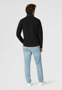 Svart tröja med texturerad baksida, figurnära stil, tillsammans med ljusblå jeans och vita sneakers. Enkelt och sömlöst design.