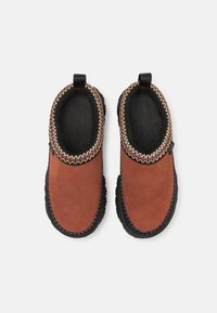 Barna velúr, slip-on cipők fekete gumi talppal, struktúrált éllel és díszítő varrással a gallér körül.