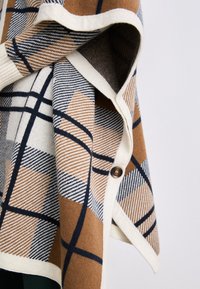 Poncho în carouri, de culoare maronie, crem și albastră, având modele geometrice, țesătură texturată și închidere cu buton la gât.