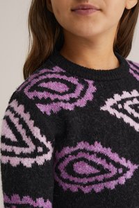 Mīksts melns džemperis ar purpursarkaniem un gaiši rozā ģeometriskiem rakstiem. Apļa kakla dizains ietver tekstūrētu dziju un kontrastējošas krāsas.