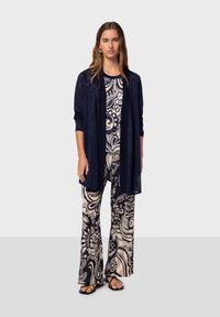 Lång marinblå kofta över en mönstrad krämfärgad topp och vida byxor. Outfitsen har blommönster och mjuka, lätta tyger.