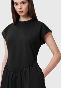 Vestido de algodón negro con un cuerpo ajustado, mangas cortas y una falda fruncida. Incluye bolsillos laterales y una textura suave.