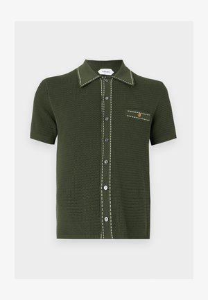 Σκούρο πράσινο πλεκτό πόλο με κοντό μανίκι, λευκή ραμμένη επένδυση, κουμπωτό εμπρός και μικρή τσέπη με χρυσό κουμπί.