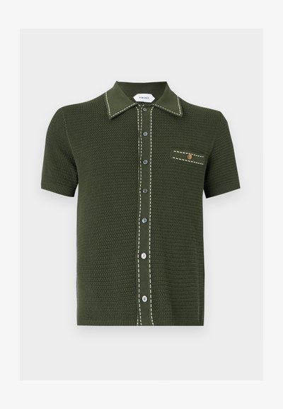 Σκούρο πράσινο πλεκτό πόλο με κοντό μανίκι, λευκή ραμμένη επένδυση, κουμπωτό εμπρός και μικρή τσέπη με χρυσό κουμπί.