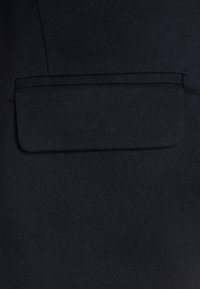 Navy tyg närbild med en strukturerad yta och en rektangulär ficka som är markerad av sömmar, vilket betonar dess skräddarsydda design.