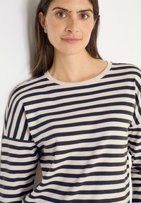 Top z długim rękawem wykonany z miękkiego materiału, zdobiony poziomymi paskami w kolorze granatowym i kremowym, z okrągłym dekoltem i luźnym krojem.