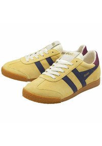 Zapatillas de ante amarillas con rayas azul marino, cordones blancos, suela de goma texturizada y acentos en burdeos en el talón.