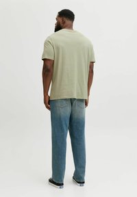 Camiseta de algodón verde claro con un corte relajado, combinada con jeans de mezclilla azul deslavado. El conjunto presenta un corte clásico y un diseño minimalista.