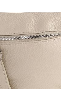 Beige leren handtas met een getextureerd oppervlak, een bovenste ritssluiting met metalen beslag en een contrasterende gestikte rand.