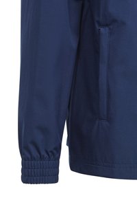 Veste bleu marine avec des poignets élastiques, texture lisse et poches latérales. Design minimaliste, matériau résistant à l'eau et sans motifs visibles.
