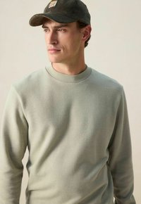 Lichtgroene sweatshirt met een ronde halslijn, voorzien van een zachte textuur. Gecombineerd met een donkergroene corduroy pet, die een subtiel ontwerp laat zien.