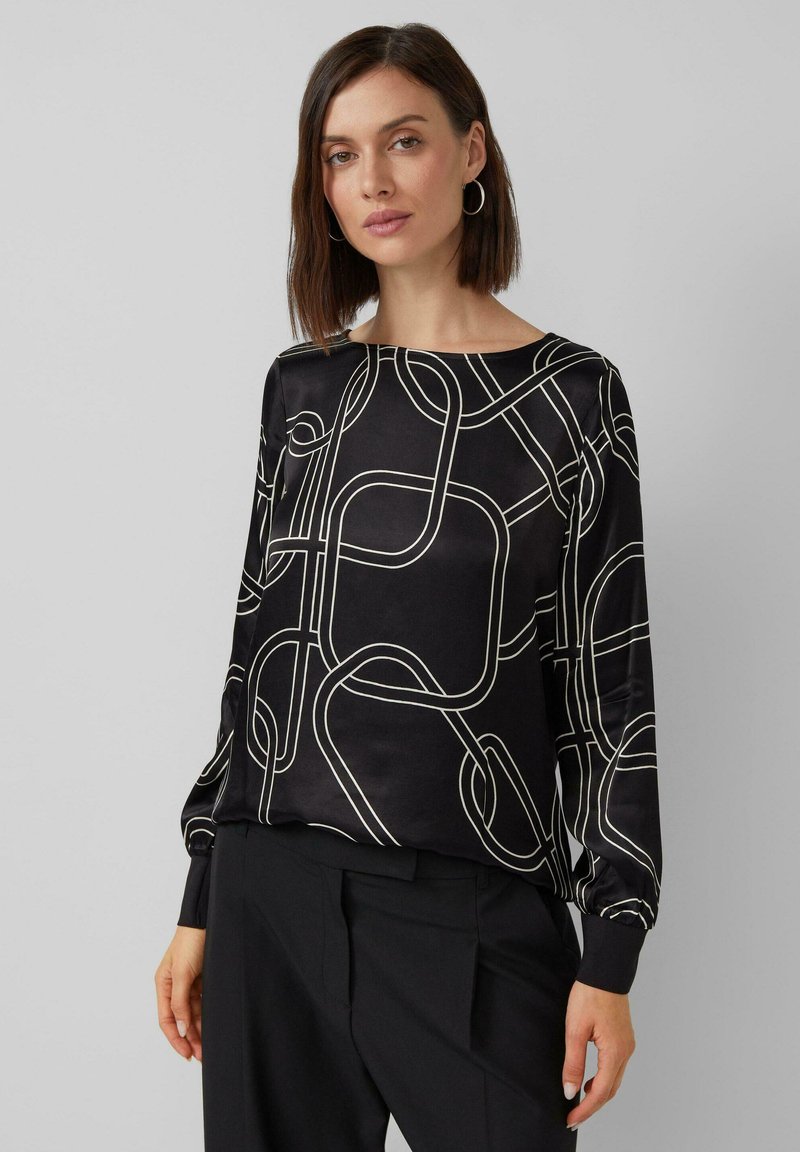 Schwarze Bluse mit einem fließenden Design, das weiße abstrakte Linien zeigt. Lange Ärmel mit enganliegenden Manschetten. Glatte, glänzende Textur.