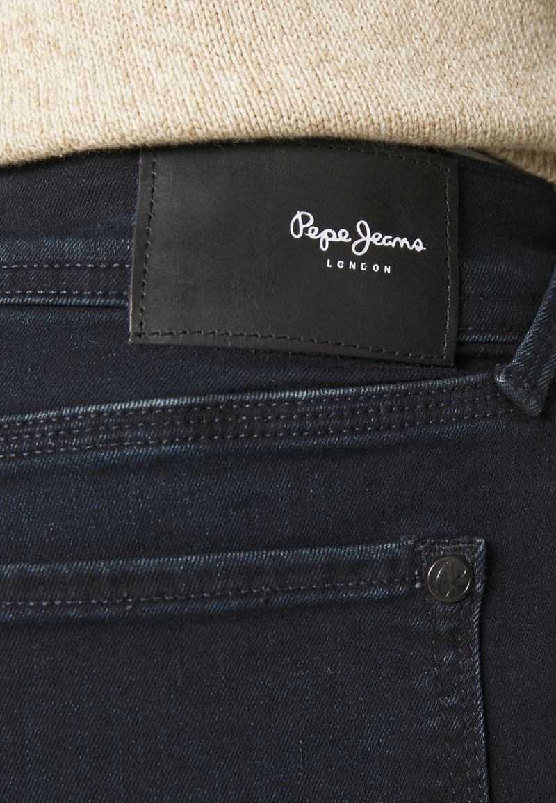 Dunkelblaue Denim-Jeans mit einem schwarzen Lederetikett mit der Aufschrift "Pepe Jeans London". Enthält sichtbare Nähte und ein Metallknopfdetail.