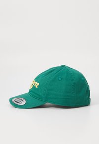Casquette en coton vert avec un bort arrondi, ornée d'un texte brodé jaune sur le devant et de six œillets de ventilation sur la couronne.