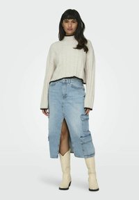 Beige ribbed cropped sweater with black trim, paired with a light blue denim skirt featuring a front slit and cargo pockets. White cowboy boots.