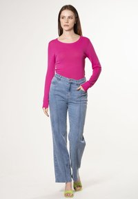 Maglietta aderente rosa a maniche lunghe, jeans in denim azzurro chiaro a vita alta con cuciture frontali, e sandali con tacchi aperti verdi.