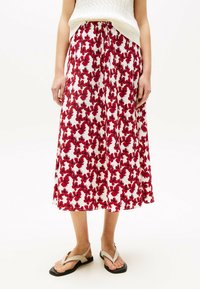 Bloemen maxi rok met een witte basis en een rood bloemenpatroon. Lichtgewicht stof, elastische taille, vloeiende ontwerp. Gecombineerd met beige sandalen.