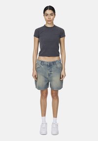 Maglietta grigia a maniche corte con colletto rotondo, abbinata a pantaloni corti in denim azzurro chiaro dal fit rilassato e design a cinque tasche. Sneakers bianche completano il look.