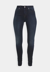 Kõrge vöökoht ja tumedat sinist värvi skinny-fit teksad, millel on ees olev nupuvajutus, klassikaline viie-tasku disain ja kerged pleekimised reitel.