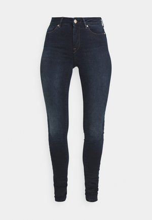 Aukštos juosmens tamsiai mėlyni džinsai, šiek tiek prigludusi forma, su priekyje esančiu mygtuko užsegimu, klasikiniu penkių kišenių dizainu ir subtiliu pablukimu ant šlaunų.