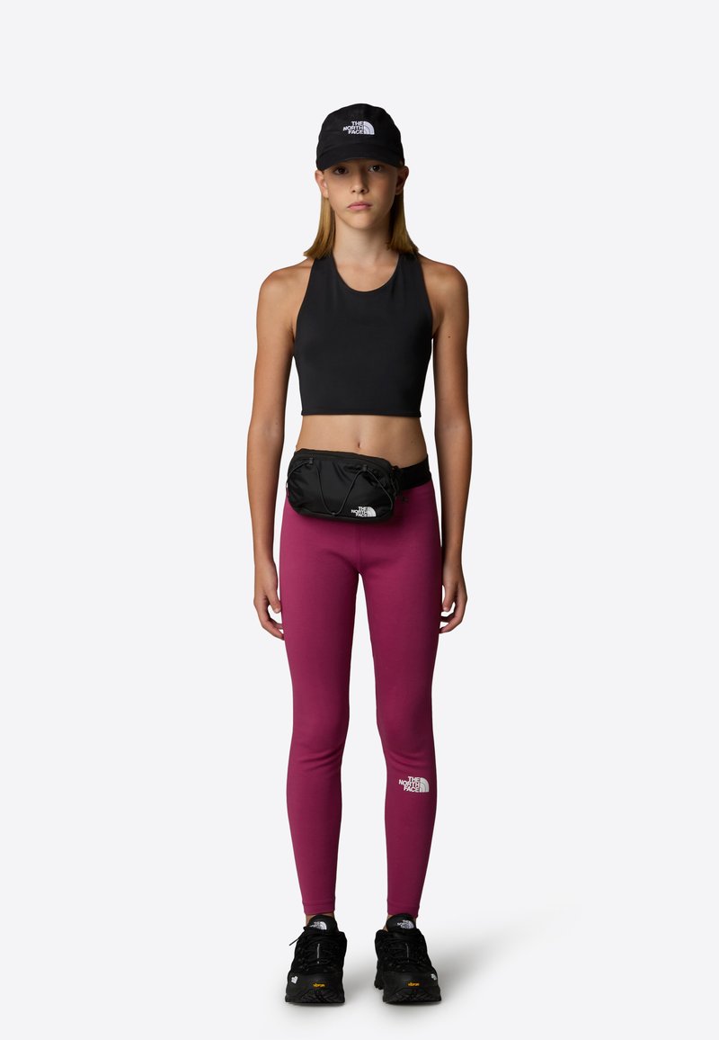Top corto nero, leggings bordeaux e borsa a vita nera. Cappellino nero con logo bianco. Scarpe nere con suole testurizzate. Posizione in piedi.