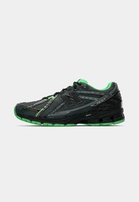 Chaussure de sport noire avec une tige en mesh texturé, accents verts, détails réfléchissants et semelle en caoutchouc noir avec un revêtement vert pour une meilleure adhérence.