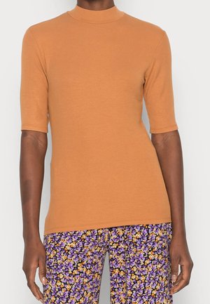 Ribbets, kortærmet top i brun; har en høj hals. Kombineret med lilla bukser med blomsterprint. Glat tekstur over det hele.