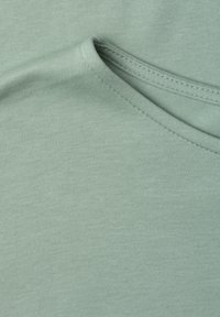 Gros plan de tissu en coton doux vert clair avec des coutures fines visibles le long d’un bord de couture plié.