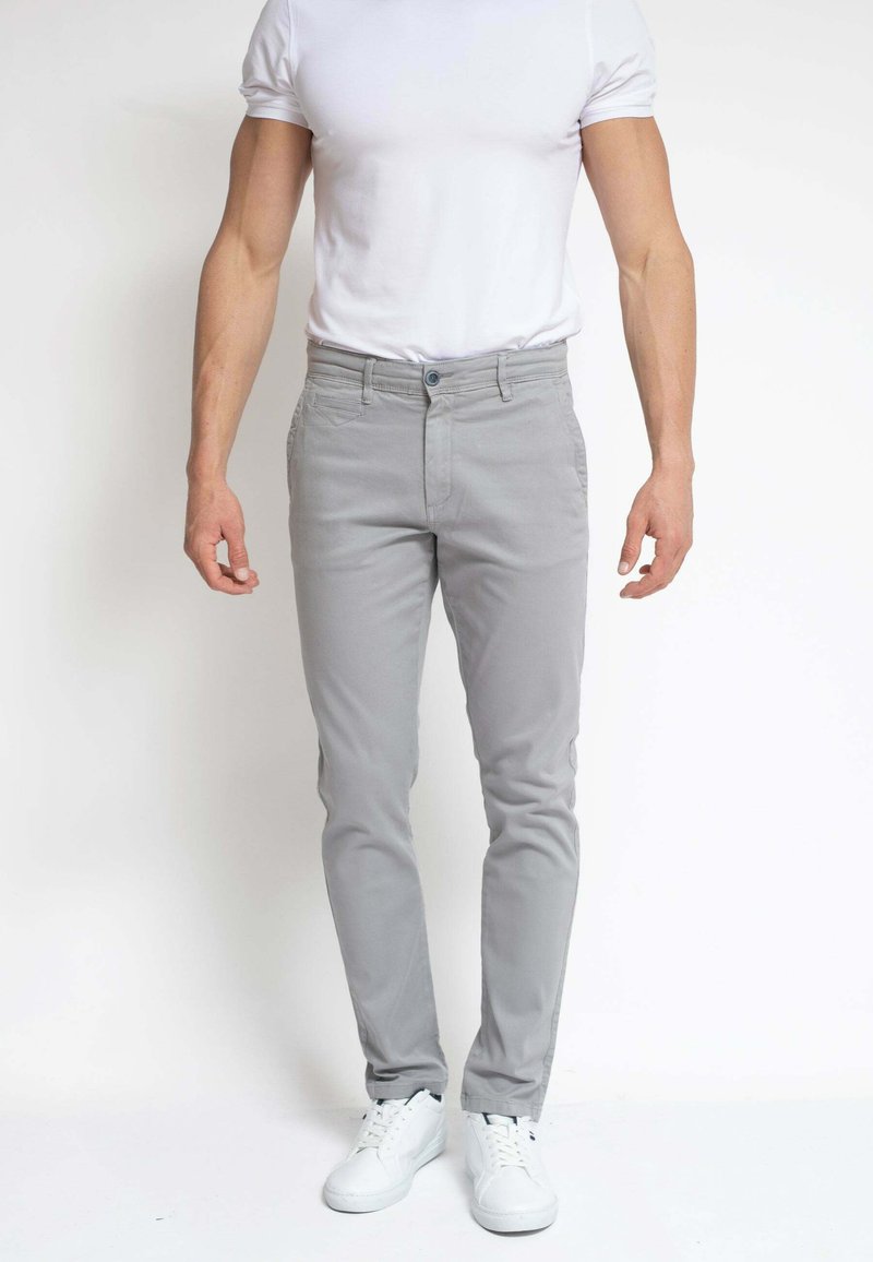 Pantalones slim-fit de color gris claro, hechos de una mezcla de algodón, con cierre de botón, bolsillos frontales y combinados con zapatillas blancas.