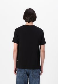 T-shirt noir à manches courtes avec un col rond et une coupe décontractée, fabriqué en tissu doux, vu de dos sur un fond blanc uni.