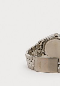 Rustfrit stål armbåndsur med et kædearmbånd, rund kasse og sølvfarvet finish; har en spænde med indgraveret logo.