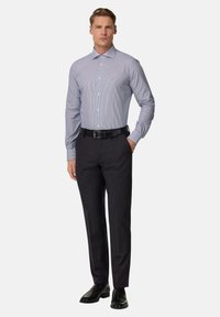 Moška srajca z gumbi v svetlo modri barvi s tankimi črtami, v kombinaciji s temnimi hlačami, črnim pasom in svetlečimi črnimi čevlji. Gladek material, prilagojen kroj.