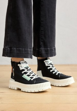 Zwarte high-top sneakers met witte rubberen zolen, gestructureerde stof, groene en oranje accenten, en witte veters. Gedetailleerde stiksels aan de zijkanten.