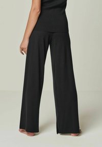 Schwarze, weit geschnittene Hose aus einem weichen, strukturierten Stoff. Mit einer hohen Taille und seitlichen Schlitzen am Saum für zusätzliche Bewegungsfreiheit.