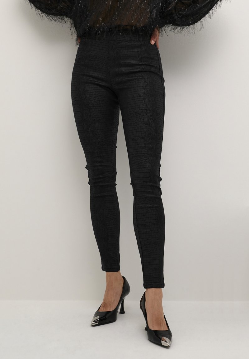Leggings en simili cuir noir avec une texture crocodile, taille haute, coupe moulante et finition brillante, associées à des escarpins noirs à bout pointu.