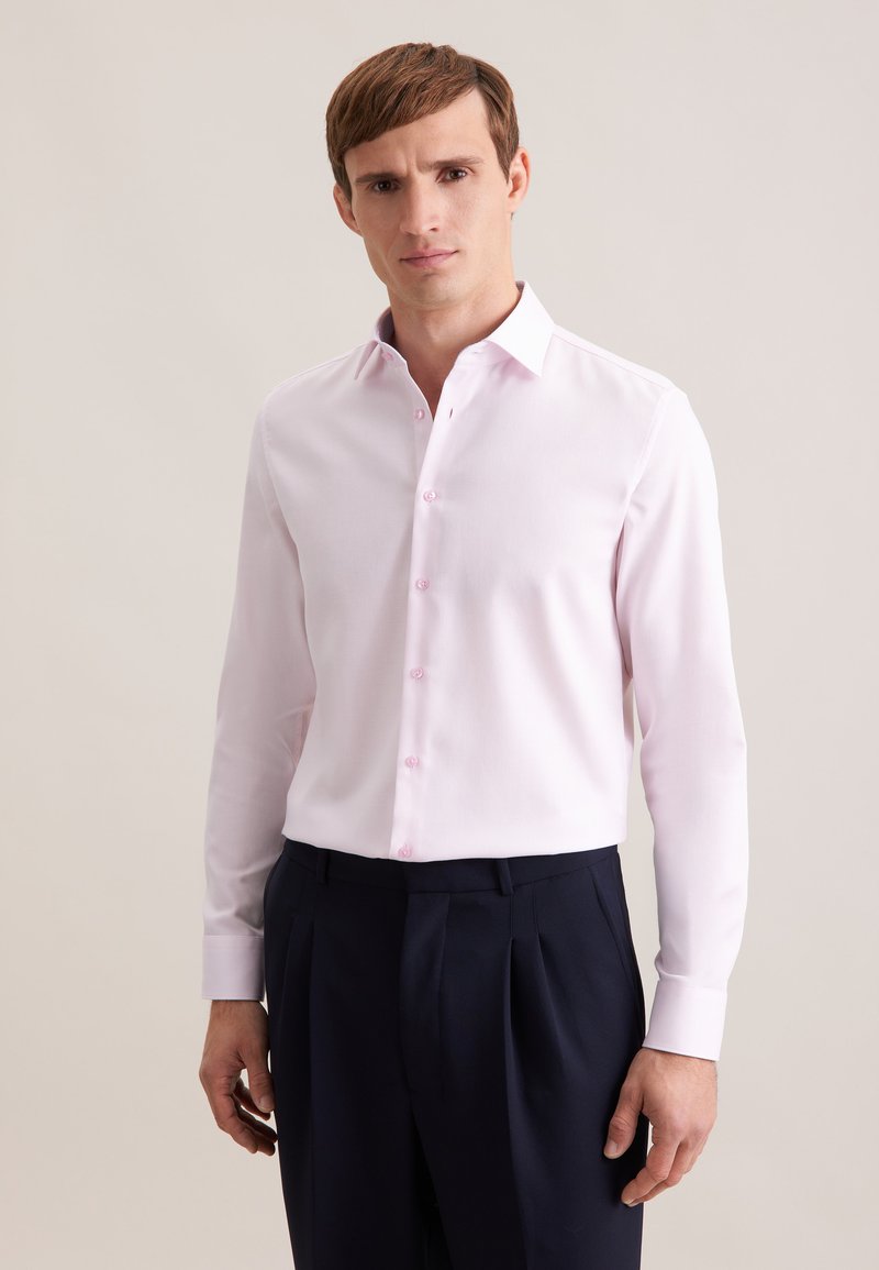 Camicia rosa chiaro a maniche lunghe con colletto appuntito, taschino frontale singolo e bottoni rosa, abbinata a pantaloni scuri su misura.
