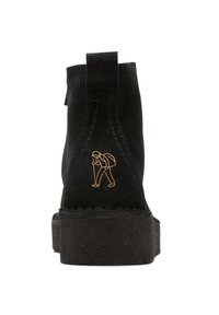 Mustat mokkanahkaiset nilkkurit, joissa on paksu pohja, teksturoitu viimeistely ja takana kultainen vaellusfiguuri kirjailtuna.