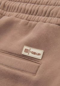 Braune Baumwollshorts mit einem strukturierten, elastischen Bund, versehen mit einem weißen Etikett mit der Marke "Level Up" auf der linken Vorderseite der Tasche.