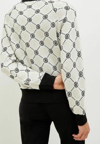 Leichter Pullover mit Musterdesign in Weiß und Schwarz, versehen mit kreisförmigen Motiven, gerippten Bündchen und Rundhalsausschnitt. Weiche Textur.