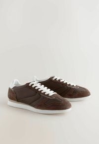 Zapatillas de ante y cuero marrón con cordones y detalles en blanco. Cuentan con un cuerpo texturizado y una suela de goma contrastante.