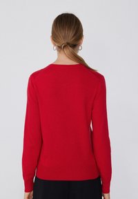 Pull rouge avec un col rond, des manches longues et un ourlet côtelé. Texture douce, design simple sans motifs ni accents visibles.