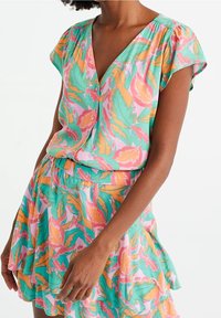 Sukienka krótko rękawowa z dekoltem w kształcie V, ozdobiona kolorowym wzorem liści w odcieniach różu, pomarańczy i zieleni. Lekka, zwiewna tkanina z rozkloszowanym dołem.