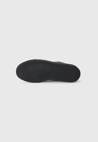 Black rubber shoe sole with a textured, ribbed pattern. The sole is flat and wide, designed for comfort and traction.