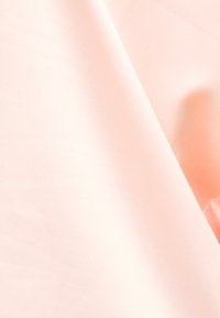 Μαλακό ροζ ύφασμα με διακριτικό δίπλωμα και μια υπόνοια ενός ροδακινί αντικειμένου στη δεξιά άκρη, δημιουργώντας απαλά σκιές και ανταύγειες.